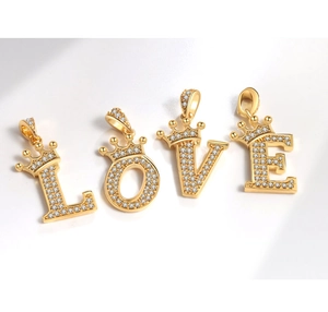 Dettaglio di ciondoli LOVE dorati con zirconi incastonati e piccoli elementi a corona