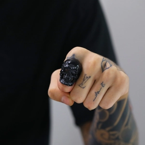 Detail of a bold black skull ring in punk style worn on a hand with artistic tattoos