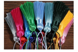Close-up of colorful silk tassels in various shades arranged on dark wood for DIY crafts