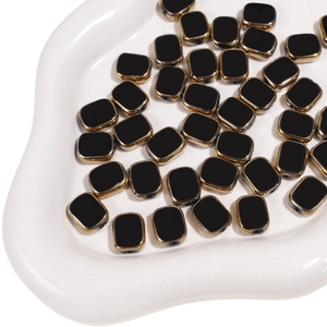 Macro shot of 10x12mm black glass beads with gold edges on white ceramic tray
