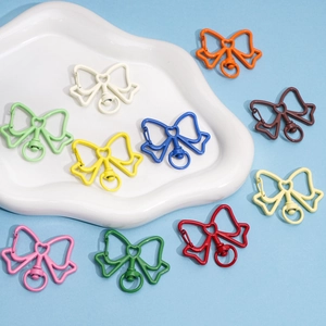 Colorful bow-shaped alloy keychains in 10 matte finishes on a ceramic tray detail