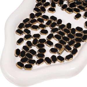 Macro shot of black octagonal glass beads with gold edges on white textured tray