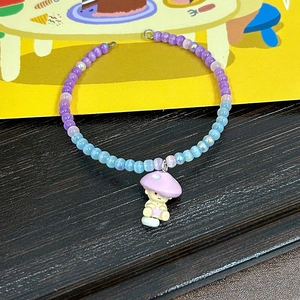 Détail d'un bracelet en perles avec breloque champignon mauve et perles irisées