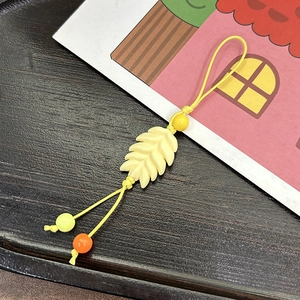 Macro shot of yellow leaf charm with acrylic beads and woven cord on wood background