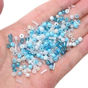 Mixed blue and white glass seed beads and tube beads held in palm for DIY jewelry