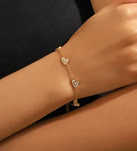 Detail eines vergoldeten Kettenarmbandes mit weißen Herzanhängern am Handgelenk