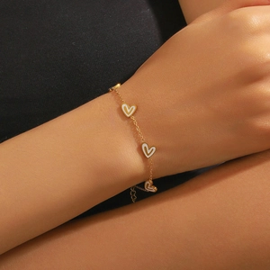 Elegantes vergoldetes Kettenarmband mit weißen Herzanhängern am Handgelenk einer Frau