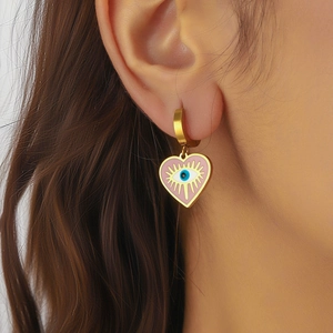 Roze hartvormige boze oog oorbellen verguld gedragen door een model voor een trendy look
