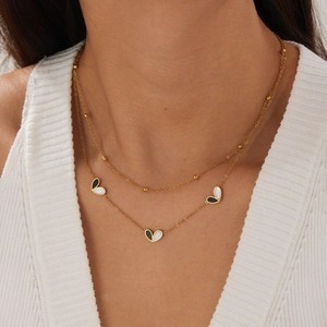 Close-up of double-layered gold necklace with black and white heart pendants on a model