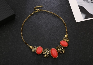 Close-up of vintage hollow oval charms and red gemstone pendants on gold chain necklace