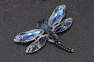 Détail d'une broche libellule ornée de cristaux bleus et strass sur fond noir brillant