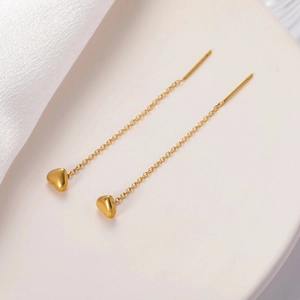 Detailed close-up of golden heart-shaped long chain tassel earrings on a soft white background