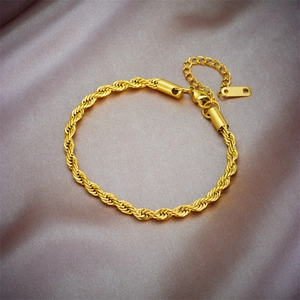 Détail d'un bracelet chaîne torsadée dorée avec fermoir mousqueton sur soie violette