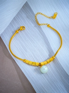Detail view of gold snake chain bracelet with white pearl pendant and square metal beads