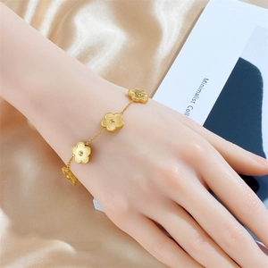 Bracelet élégant en or avec breloques fleurs à cinq pétales porté sur fond de soie