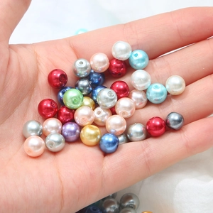 Hand holding assorted colorful glass faux pearl beads with hole for DIY jewelry making