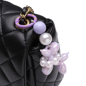 Detail of black quilted shoulder bag with unique purple balloon dog charm and pearls