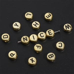 Close-up of 4x7mm gold acrylic alphabet beads with black letters spelling NICE on a pin