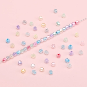 Faceted macaron glass beads for DIY jewelry making displayed on a soft pink background