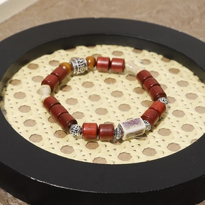 Detalle de pulsera étnica de madera con cuentas cilíndricas rojas y toques plateados