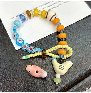 Detail eines bunten Perlenarmbands mit handgemalten Keramikvögeln und einem Baseball-Element