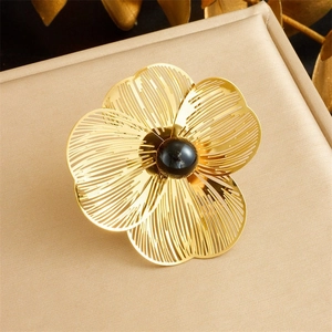 Detail of a hollowed gold flower brooch with a black pearl center on silk texture
