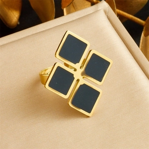 Detail of a gold-plated ring with four black square motifs on a satin jewelry stand