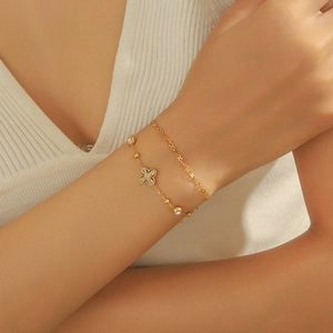 Détail d'un bracelet double chaîne dorée avec pendentif trèfle et perles polies