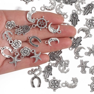 Assorted vintage silver alloy charms for DIY jewelry making shown in hand for scale