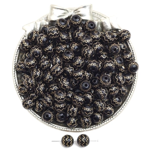 Macro detail of vintage black acrylic beads with gold wave patterns on a silver tray