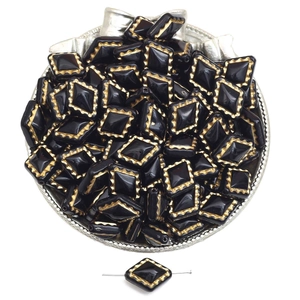 Macro detail of black and gold acrylic rhombus beads in a silver tray for DIY jewelry