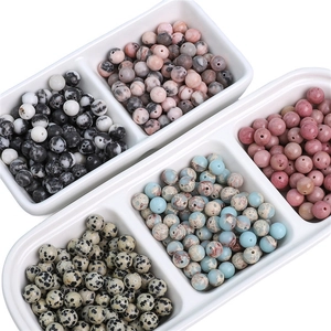 Macro shot of 8mm natural Dalmatian Jasper and Rhodonite loose beads in white tray