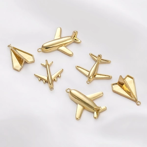 Detailed view of 14K gold-plated airplane and paper plane charms on white silk fabric