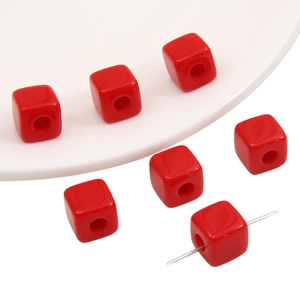 Close-up of red acrylic cube beads for DIY jewelry making with a needle through one bead