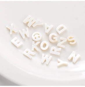 Macro detail of white iridescent shell letter beads for DIY jewelry making in a bowl