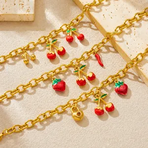 Gros plan détaillé du bracelet en chaîne dorée avec charms fraise et cerise sur sable