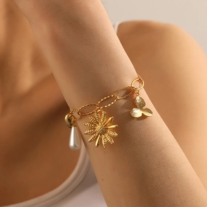 Detail of gold-plated chain bracelet with white pearl, daisy and leaf charms on wrist