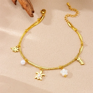 Detail of gold beach anklet with starfish and shell charms over a sandy backdrop