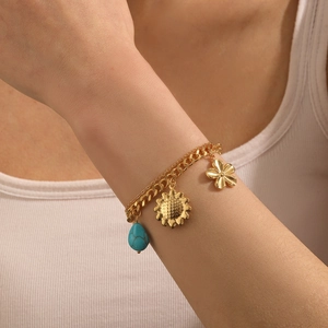 Detail of gold layered bracelet with sunflower, flower charms and turquoise bead