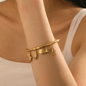 Detail of gold bamboo texture bangle with sea star shell whale and seahorse charms
