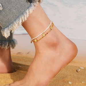 Double-layered daisy bead anklet with gold chain on a sunny summer beach setting