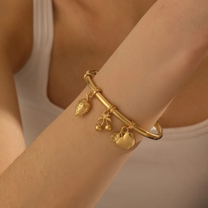 Detail of gold-plated bamboo bracelet with strawberry, cherry, and apple charms on wrist