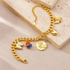Detail of gold Cuban link bracelet with bee, heart and flower charms on stone surface