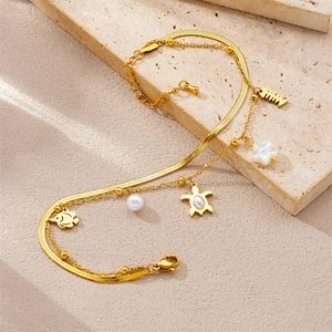 Detail of gold double-layer anklet with starfish, fishbone, and shell charms on stone