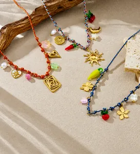 Detail of bohemian colorful woven necklaces with heart, sun and cherry pendants on sand