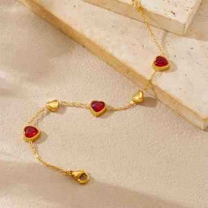 Vue détaillée du bracelet cœur doré avec strass rouges sur fond de pierre beige clair