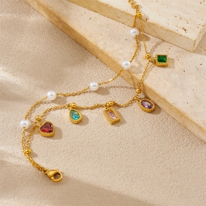 Detail van de goudkleurige armband met gekleurde edelsteenhangers en witte parels