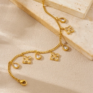 Detail van vergulde ketting met klaverhangers en druppelvormige kristallen op steen