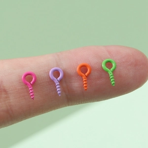 Tiny colorful spray painted eye pins for DIY jewelry making held on a fingertip