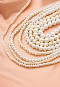 Gros plan de perles d'imitation blanches de tailles variées sur un tissu satin rose